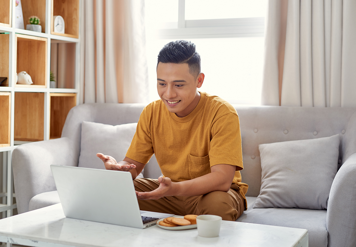 smiling man in a casual shirt, looking down on a laptop, talking to someone, and making hand gestures